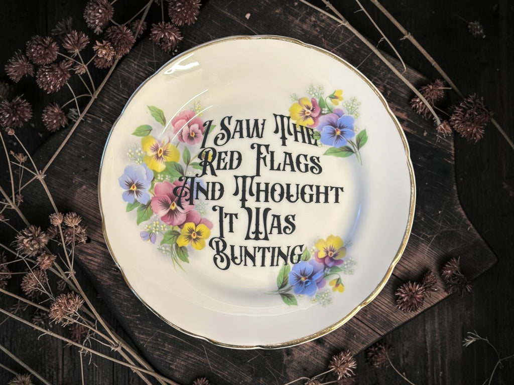 Vintage decorative plate reading I Saw the Red Flags and Thought It Was Bunting