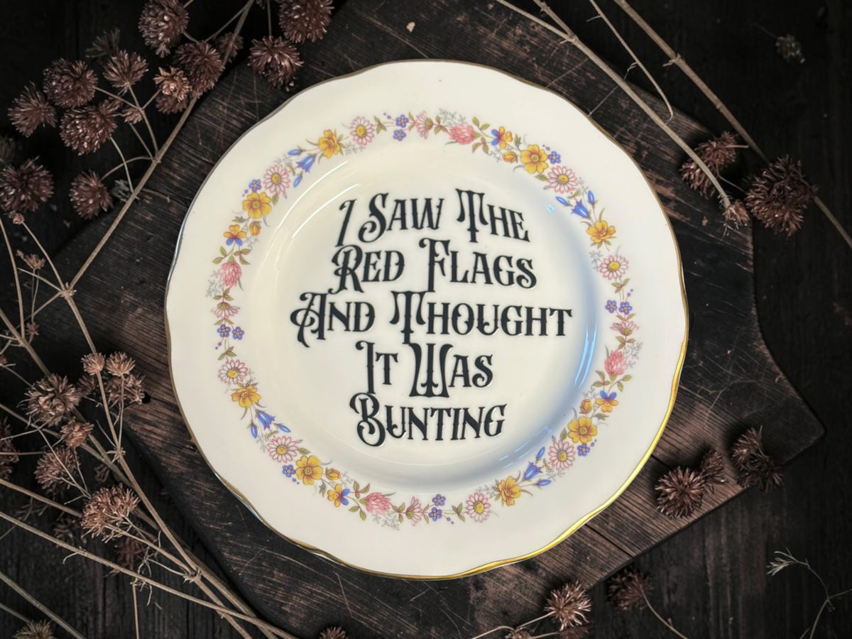 Vintage decorative plate reading I Saw the Red Flags and Thought It Was Bunting