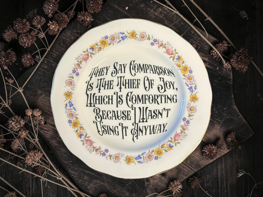 Vintage decorative plate reading They Say Comparison Is the Thief of Joy, Which Is Comforting Because I Wasn’t Using It Anyway